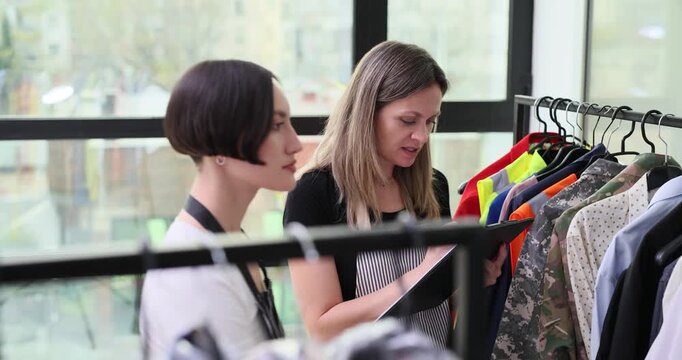 Stylist browsing new collection on rack, caucasian stylist and colleague examine silhouettes and fabrics, hands inspect seams