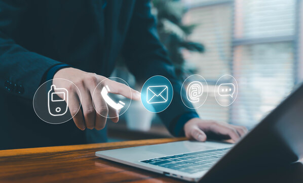 A businessman touching virtual communication icons above a laptop, representing contact methods, customer support, digital connection, and modern communication technology for business services. - Powered by Adobe