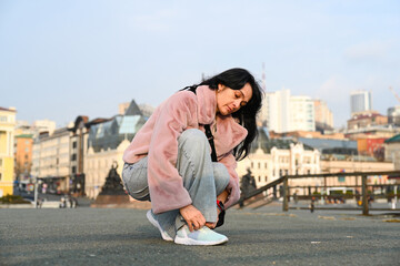 Mature 50 years old Russian woman tying her shoelace in Vladivostok, wearing a pink fur jacket and...