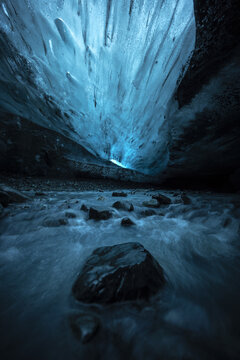 View of the surreal, cavernous ice cave, illuminated with an ethereal blue glow, the meltwater flowing over dark rocks, Vatnajokull, Iceland.