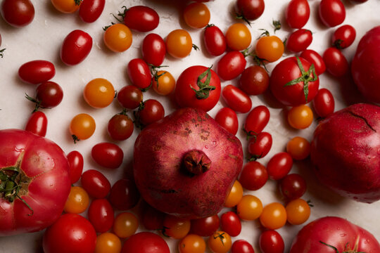 Pomegranate and assortment of red and yellow cherry tomatoes on a light marble surface - Powered by Adobe