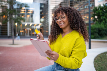 Smiling young woman shopping online using tablet outdoors