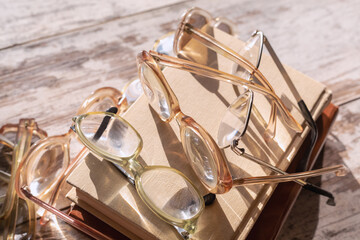 Various vintage reading glasses lie on top of books in bright sunlight with light reflections on the lenses on a wooden table, close-up. Suitable for ebook covers, courses, articles about learning