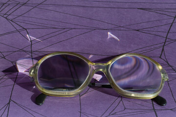 Glasses lie on a dark purple background with black chaotic lines, close-up. Book reviews, complex plots, searching for logic and solutions to difficult problems