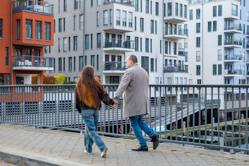 Happy young woman and man playfully running across bridge, couple holds hands, dynamic portrait active partnership, cheerful mood, lively autumn day, fun outdoor moment in modern European city