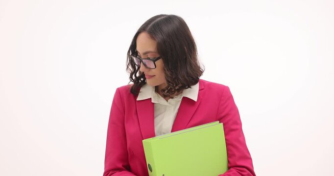 Pretty businesswoman adjusts glasses as holds ring binder on white background. Bashful female corporate employee hides eyes in office workspace