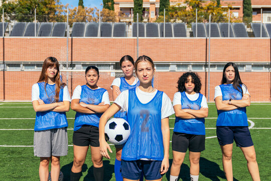 Diverse female football players posing together on a sunny outdoor sports field, representing teamwork and empowerment