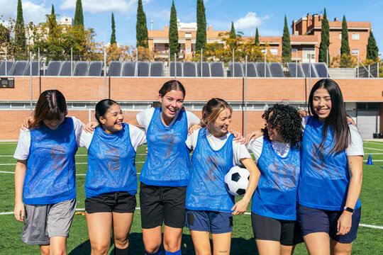 Group of happy young multiracial women soccer players standing together on a sports field, celebrating friendship and team spirit
