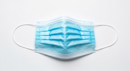 Light-blue surgical mask lies flat, white earloops & surface background