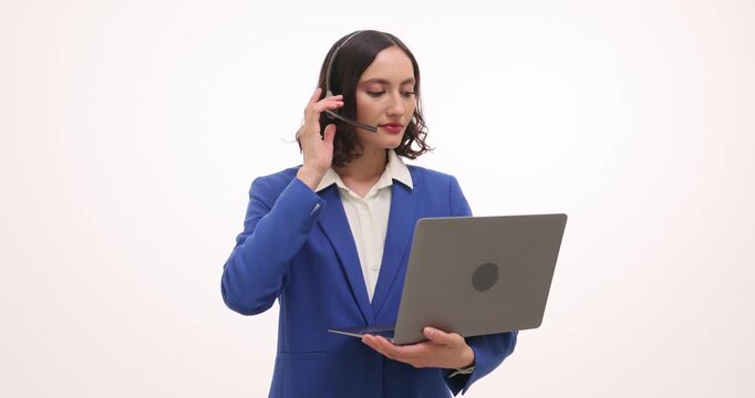 Woman call center operator in blue suit raises headset mic connecting to call. Female holds laptop and opens ticket starting customer support session