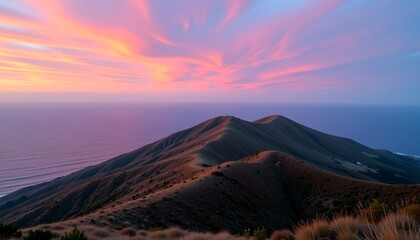 Scenic mountain range overlooking the ocean at sunset. The sky displays vibrant hues of pink, orange, and purple