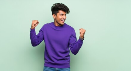 Joyful young man in vibrant purple sweatshirt celebrates a triumphant success, beaming with energetic happiness against a fresh green wall