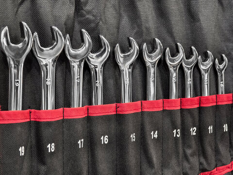 Array of shiny wrenches neatly organized in a black and red tool pouch at a workshop