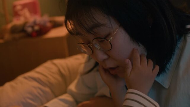 Caring Asian mother talking to her kids in bed, sharing bedtime stories and comfort before sleep in cozy warm light of child bedroom