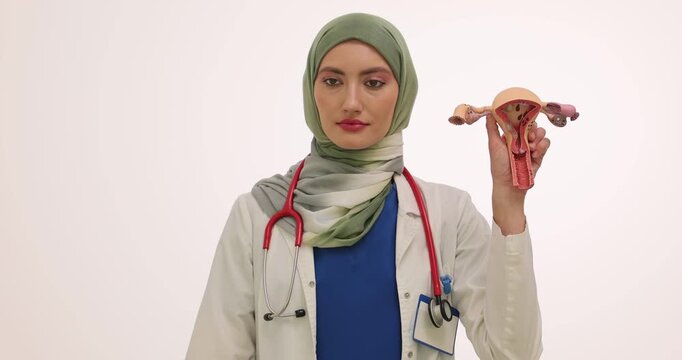 Gynecologist holds anatomical model of uterus and medical suppositories on white background. Muslim doctor discusses course of treatment. Slow motion