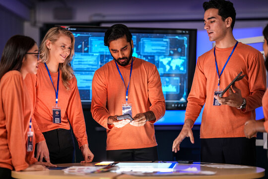 A diverse team of young innovators in a tech lab presents a new smartphone prototype, enthusiastically brainstorming its next-generation design and user interface for a future product launch.