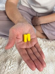 Close-up of a woman’s hand holding soft yellow foam earplugs designed for sleep improvement, noise reduction, and hearing protection