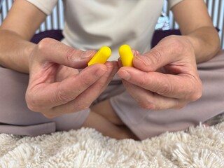 Close-up of a woman’s hand holding soft yellow foam earplugs designed for sleep improvement, noise reduction, and hearing protection
