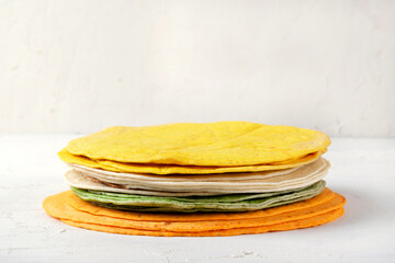 Assorted tortillas of various colors lie in a stack on a white table. Flat bread made with wheat flour with spinach, turmeric and tomato powder