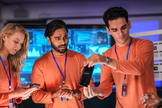 A diverse team of young innovators in a tech lab presents a new smartphone prototype, enthusiastically brainstorming its next-generation design and user interface for a future product launch.