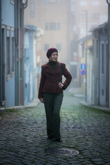 Foggy street portrait of a woman in a burgundy beret and textured coat walking along cobblestones.