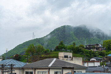 Itozaki, Japan - April 28, 2025 Misty green hillside rising behind small town rooftops under an overcast sky