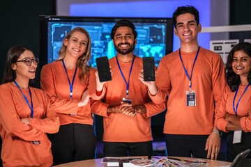 A diverse tech event team in matching orange uniforms collaborates in a high-tech control room, coordinating logistics by analyzing real-time data on a tablet and smartphone.