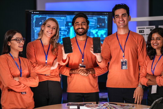A diverse tech event team in matching orange uniforms collaborates in a high-tech control room, coordinating logistics by analyzing real-time data on a tablet and smartphone. - Powered by Adobe