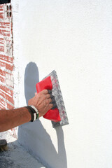 Plastering a wall with thick white paint.