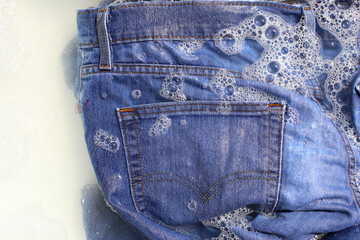A pair of blue denim jeans soaking in soapy water, creating a layer of foam.