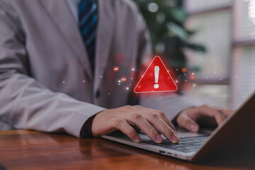 A red warning alert icon appearing above a person typing on a laptop, symbolizing cybersecurity risks, system errors, data threats, caution messages, and critical digital alerts in modern technology.