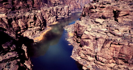 The expansive canyon showcases towering rocky cliffs with layered patterns, while a clear blue river flows gracefully between them under bright sunlight.