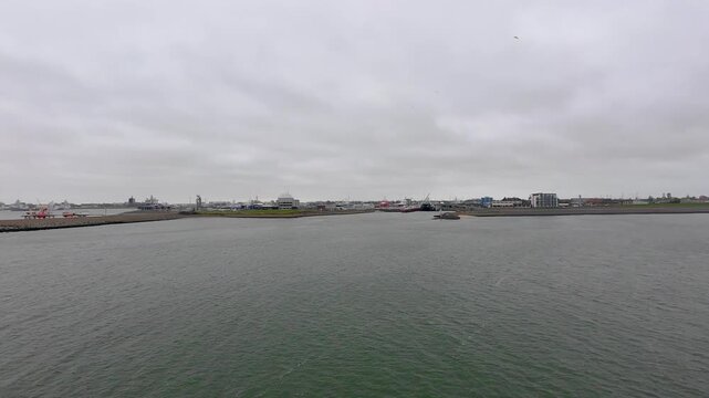 Den Helder, The Netherlands, October 25th, 2024, Overcast harbor panorama with calm water, distant industrial port, docked vessels, gentle ripples, gray skyline, overcast sky,