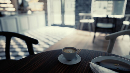 A cup of coffee sits on top of a wooden table in a modern cafe interior.
