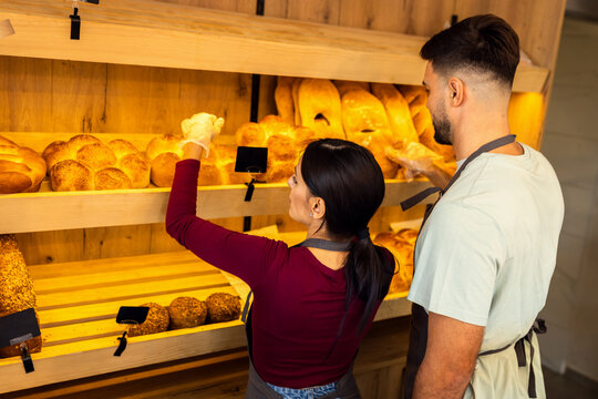 Man and woman arranging freshly baked bread on shelves inside bakery.