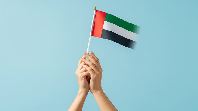 raised uae flag on blue. hands holding small united arab emirates flag up in the air on blue background - Powered by Adobe