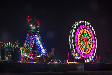 Vibrant rides in the Colorful Giant Ferris wheel with night illumination in the funfair, Maharashtra, India.