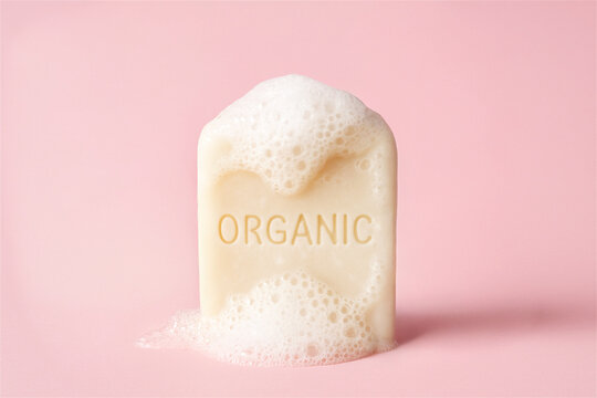 Organic skincare soap bar forming a rich lather with white bubbles, promoting natural hygiene and a clean feeling against a light pink studio background