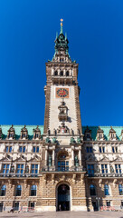 The impressive clock tower and main entrance of Hamburg City Hall (Rathaus) in Germany, captured on a clear, sunny day against a bright blue sky