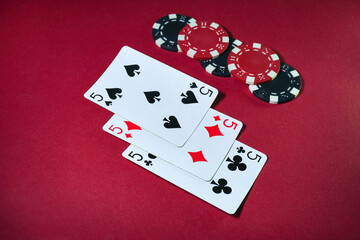 An exciting card game featuring three fives or three of a kind and colorful poker chips on a vibrant red background