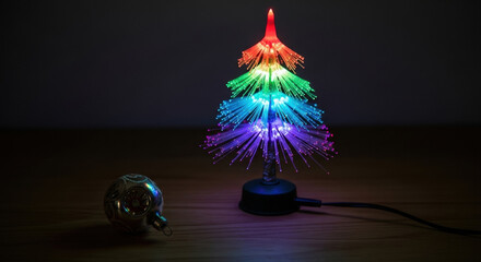 Small fiber optic tree on wooden surface changing colors. Vintage ornament and electrical cord beside the tree. Retro fibre optic Christmas tree, colorful lights, dark background