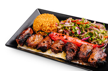 Grilled meat and rice dish with fresh vegetables served on black plate