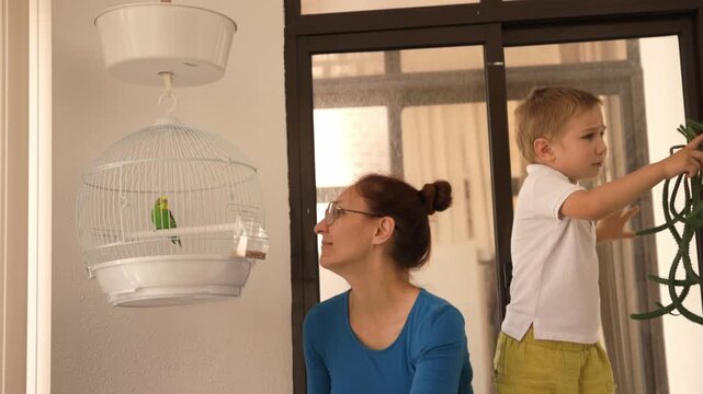 Mother and son interacting with a pet budgie in a cage