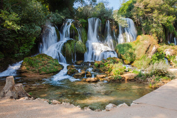 Lush Kravice Waterfalls cascade into emerald water, surrounded by dense greenery near Medjugorje, Bosnia—an idyllic natural landscape with vibrant mist and serene reflections.