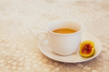 Warm cup of tea in a white ceramic mug with a fresh sliced fig on a saucer, placed on a textured stone surface in soft natural light, evoking calm, comfort, and slow living.