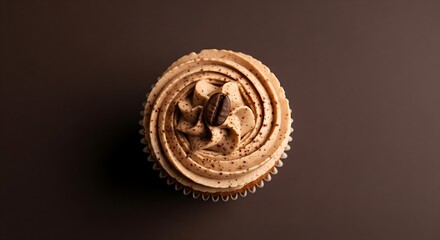 A coffee cupcake with mocha frosting and a single roasted coffee bean, isolated on a dark brown background.