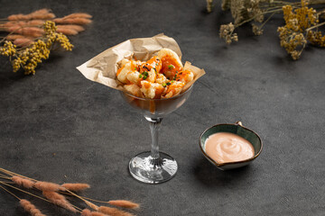 Golden crispy shrimp bites presented in glass cup with herbs and paired with creamy dipping sauce