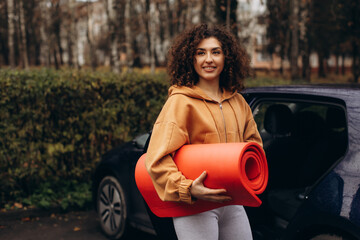 Young woman leaving car carrying yoga mat for fitness