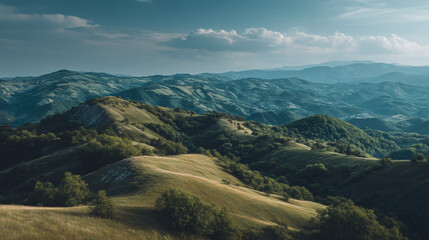 Obraz premium Aerial view of rolling hills and mountains under a blue sky with scattered clouds above