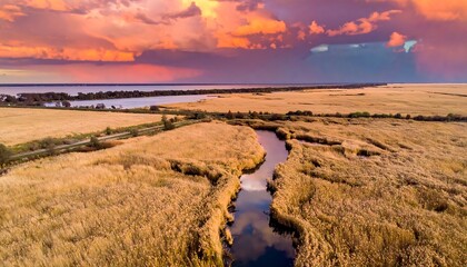 Marshy river landscape with tall grasses beneath a dramatic, colorful sunset sky, reflected in the water